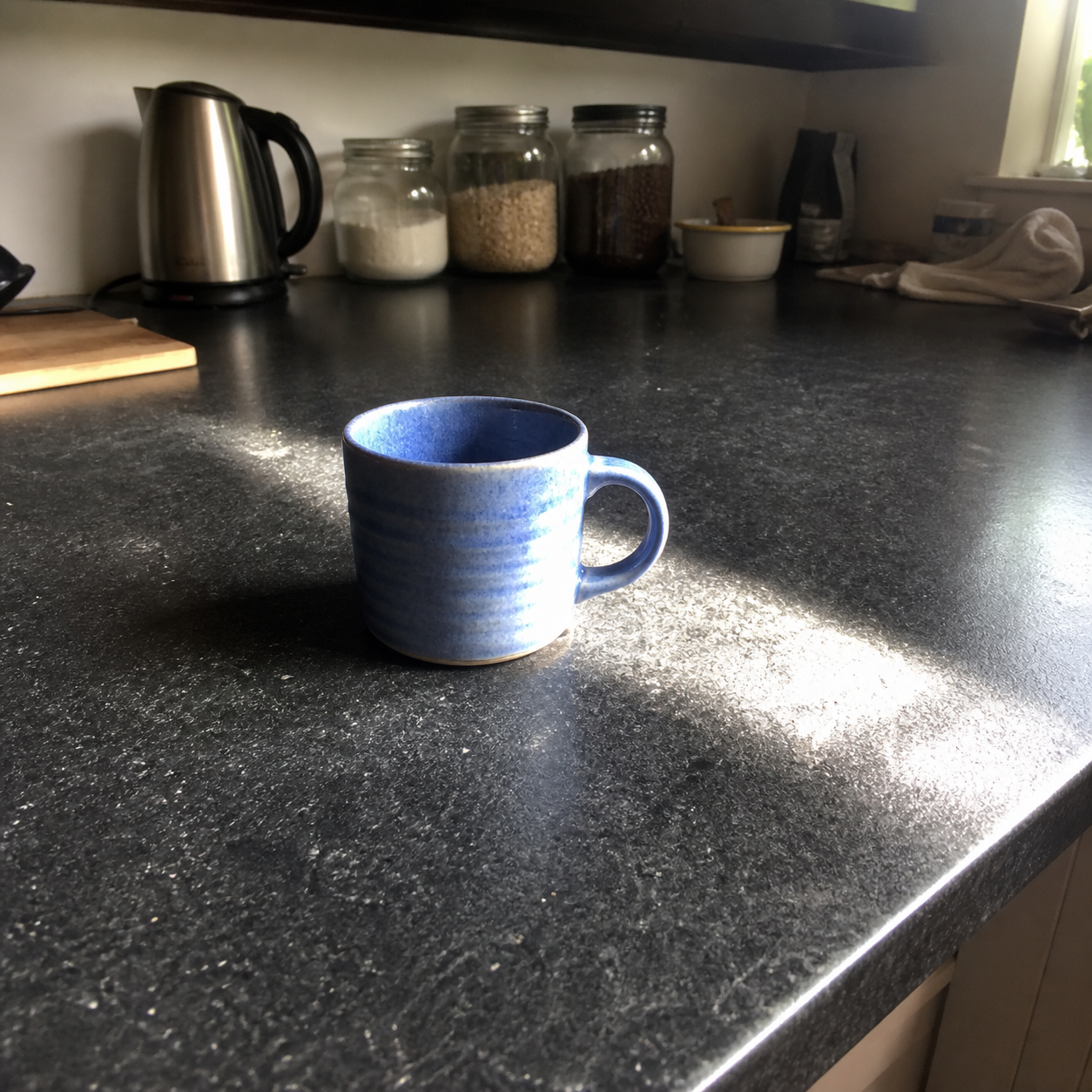 Demo photo of a speckled blue ridged stoneware mug on a dark, cluttered kitchen counter, small and off-center in the frame with harsh window glare.